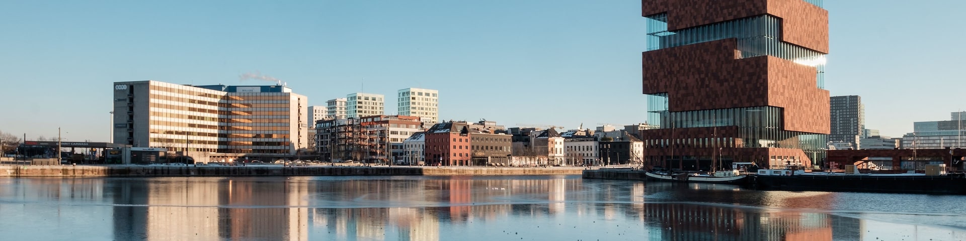 Horizonte urbano com arquitetura moderna, um corpo d'água refletindo os edifícios e céu claro.