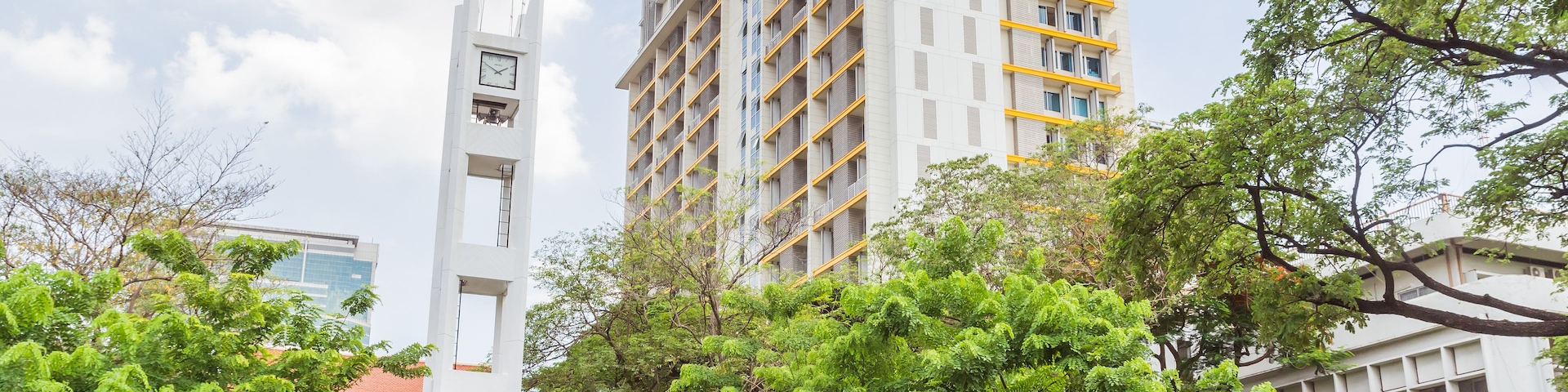 Un edificio moderno con una torre de reloj, rodeado de exuberantes árboles verdes y un cielo despejado.