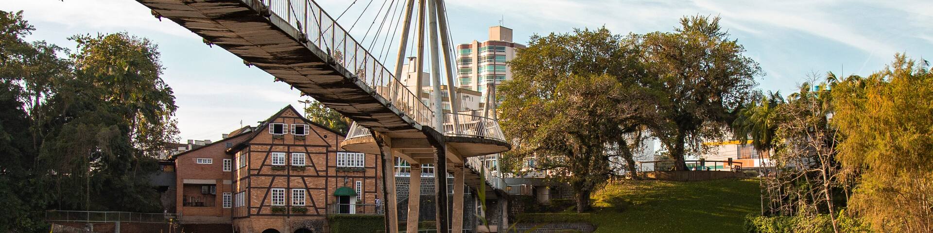 A bridge with a reflection in a calm body of water, a historic building, and trees in a park setting.