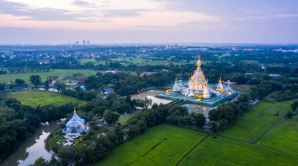 An aerial view of a temple complex with a large central building and smaller structures, surrounded by lush greenery and fields.
