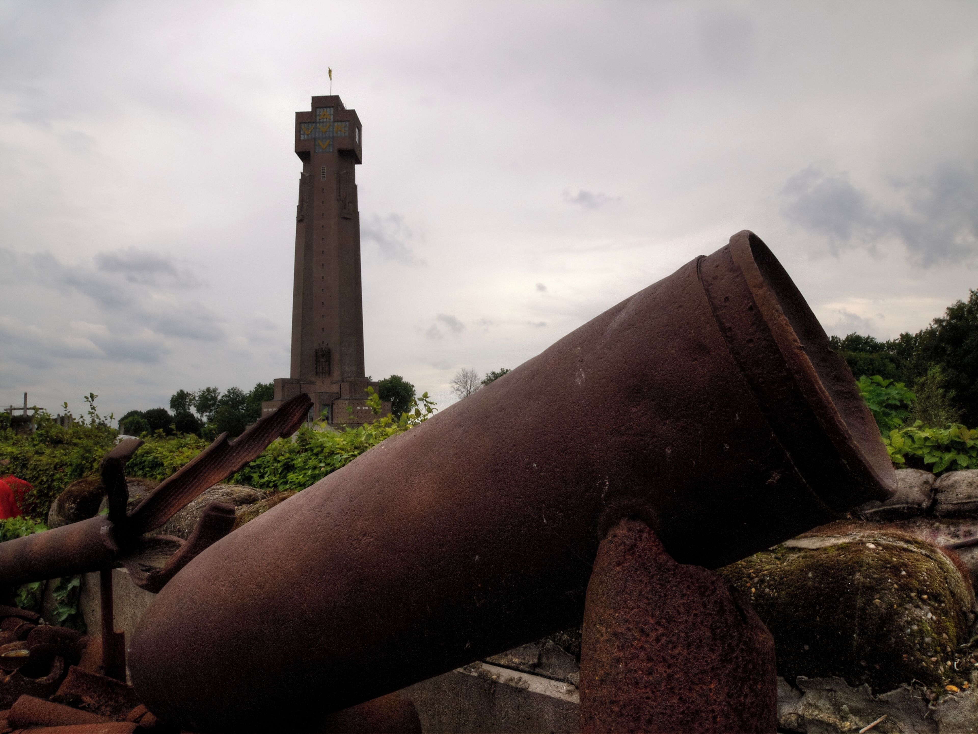 A rusted cylindrical object and a tall tower in the background.