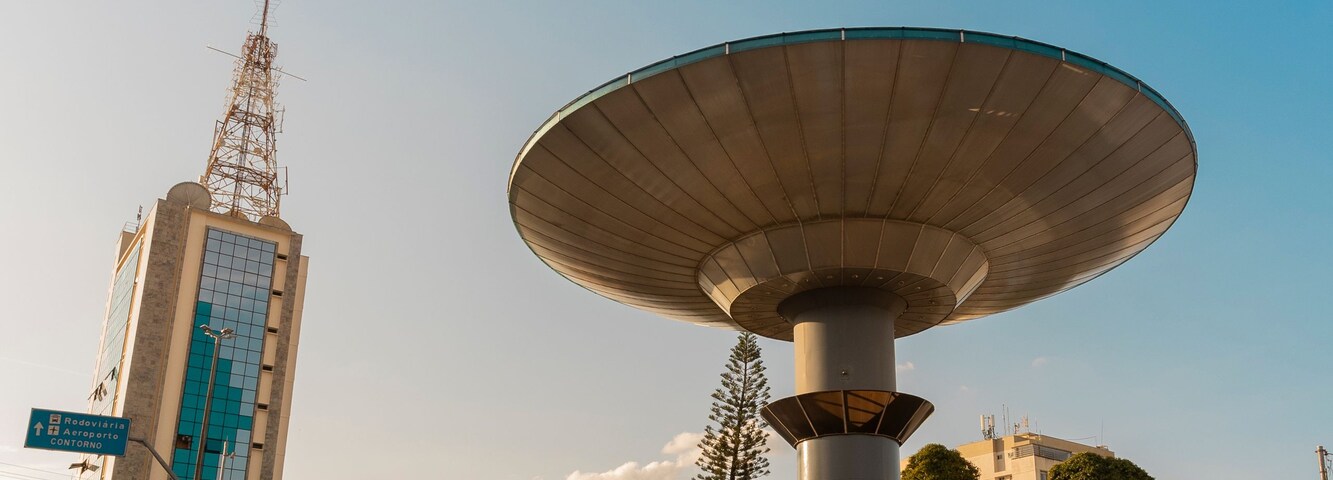 Una gran antena parabólica, un edificio alto con antenas y una carretera con vehículos.