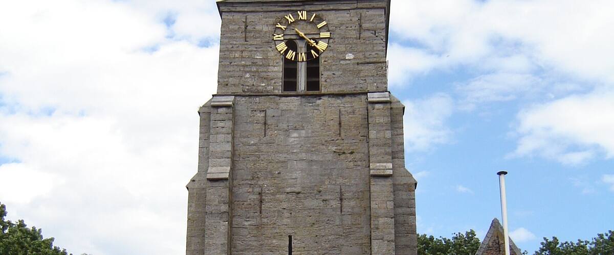 A church with a clock tower, a wooden door, and a sign that reads "Wandelpad".