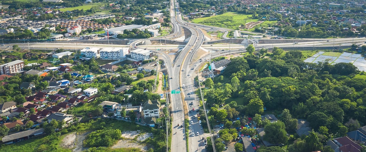 Vista aérea de una ciudad con una autopista destacada, zonas residenciales y una cadena montañosa distante.