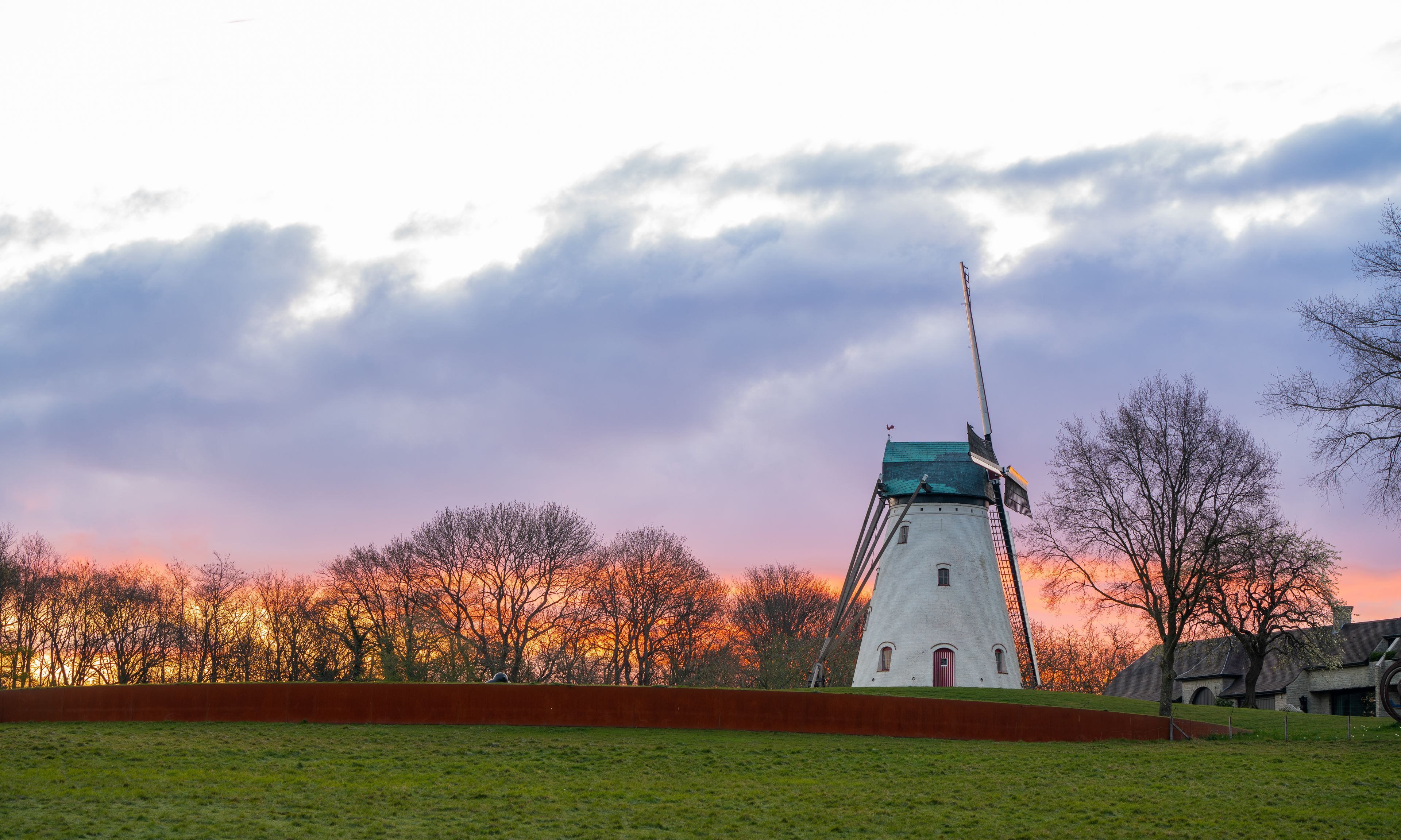 Een windmolen met een groen dak, omringd door bomen en een bewolkte lucht.