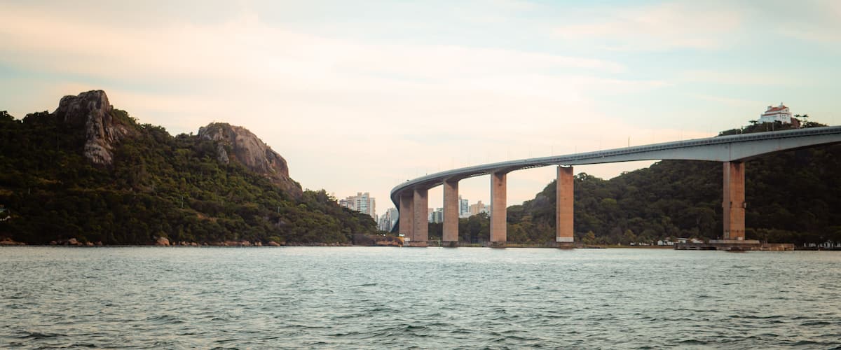 Uma ponte sobre a água, com montanhas ao fundo e um edifício no topo.