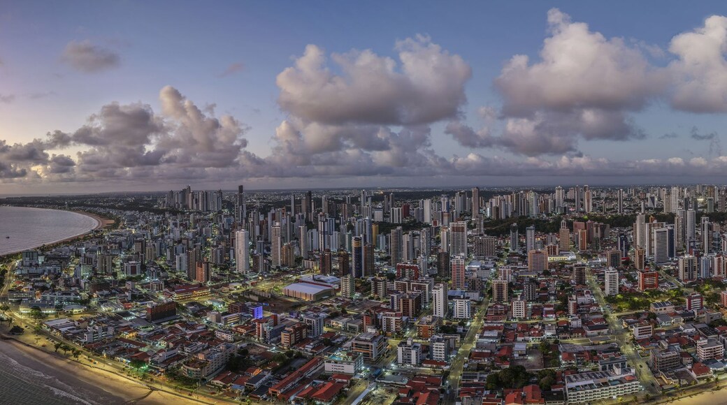 Aerial view of the coastal city of Joao Pessoa with its skyline, sandy beaches, and the Atlantic Ocean under a dramatic sunset sky in Joao Pessoa, Paraiba, Brazil.