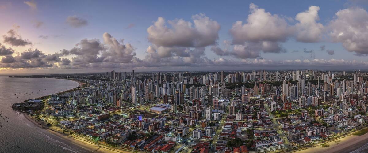 Paisagem urbana costeira com uma linha de costa sinuosa, edifícios urbanos densos e um céu ao pôr do sol.
