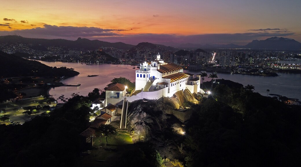 A coastal cityscape at dusk with a prominent white church on a hill, a river, and a city skyline in the background.