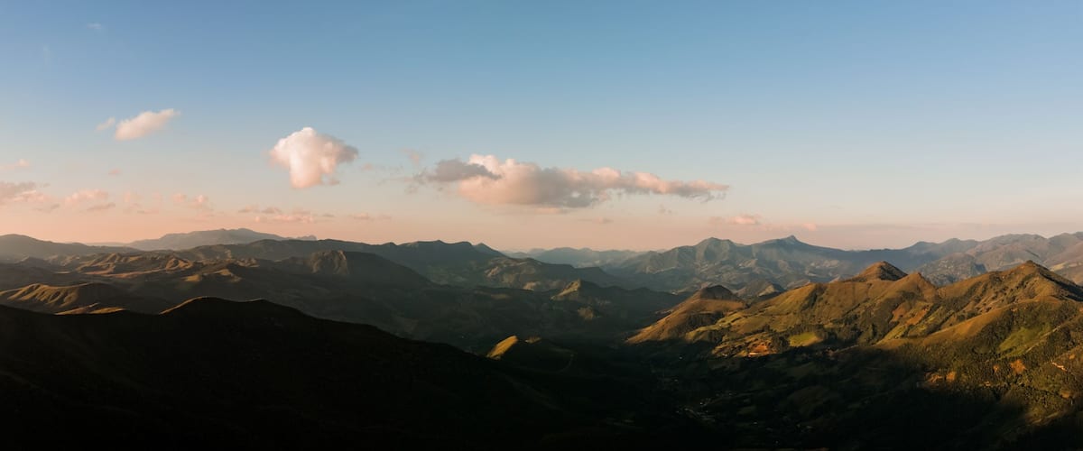 Fotografia aérea panorâmica da Serra da Mantiqueira, Minas Gerais, Brasil, com pôr do sol dourado iluminando montanhas, paisagem natural cinematográfica ideal para turismo, viagem e natureza.
