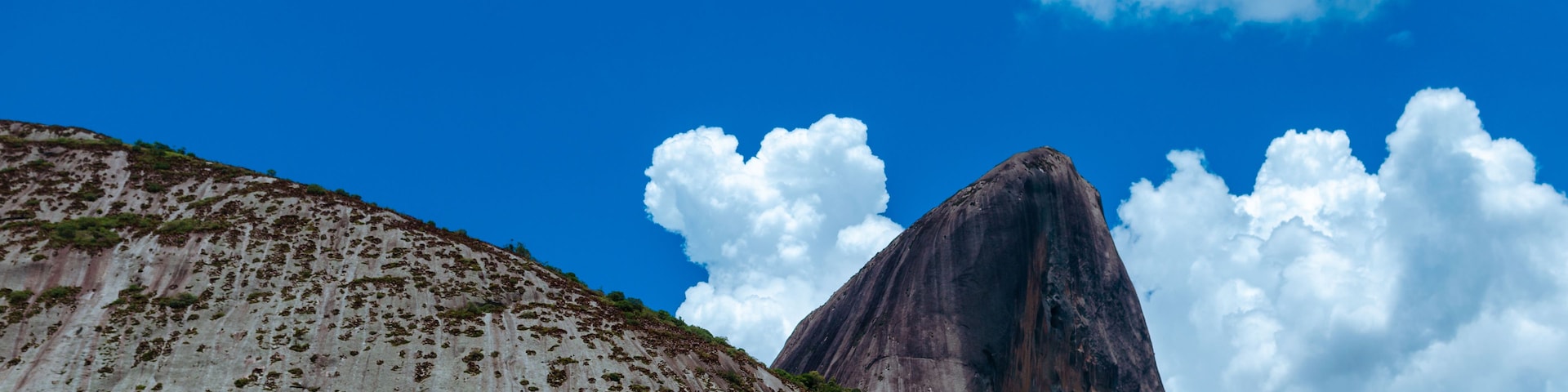 Uma montanha imponente com um pico proeminente, sob um céu azul límpido com algumas nuvens.