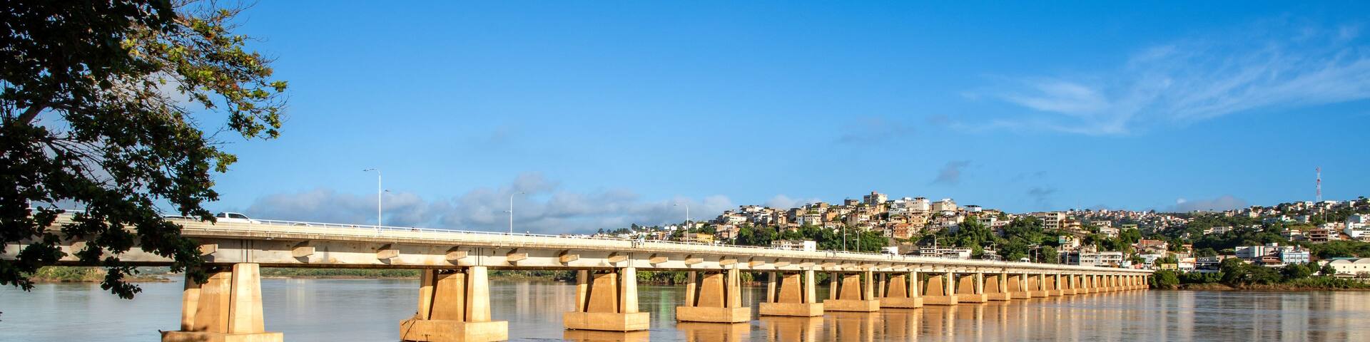 A bridge over a calm river with a cityscape in the background.