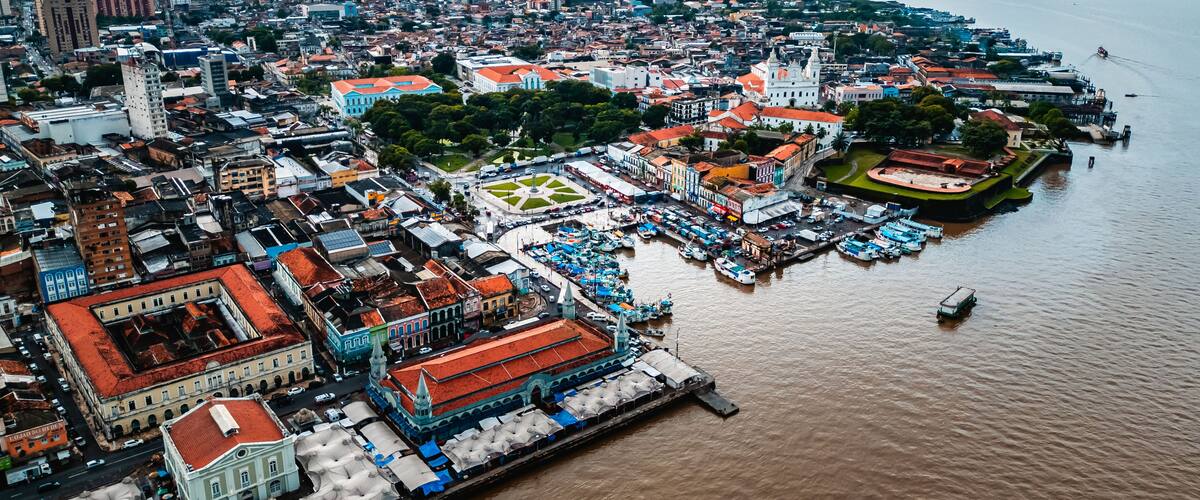 Vista aérea de una ciudad costera con un paseo marítimo destacado, edificios históricos y una gran plaza abierta.