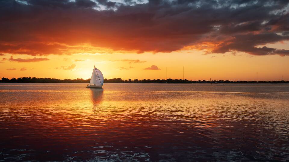 Un velero en aguas tranquilas durante el atardecer, con un cielo espectacular.