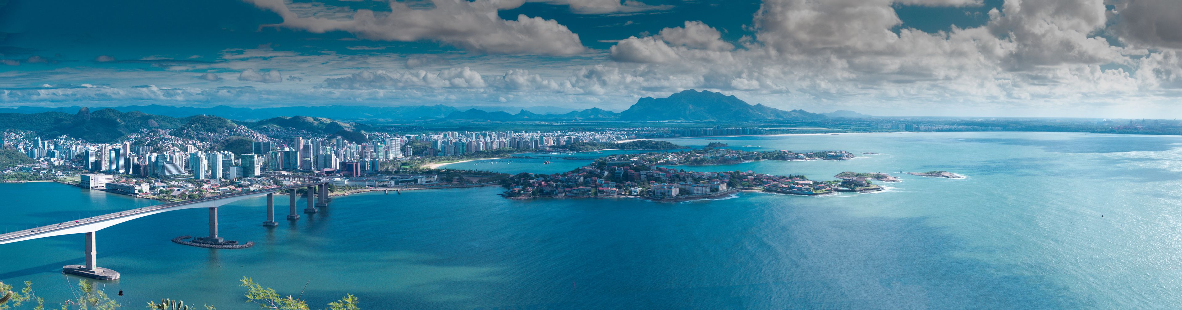 Paisagem costeira urbana com uma ponte imponente, área densamente construída e uma grande extensão de água com ilhas.