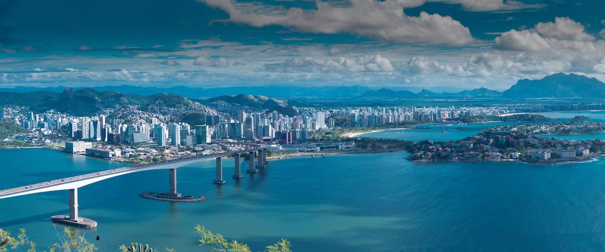 Paisagem costeira urbana com uma ponte imponente, área densamente construída e uma grande extensão de água com ilhas.