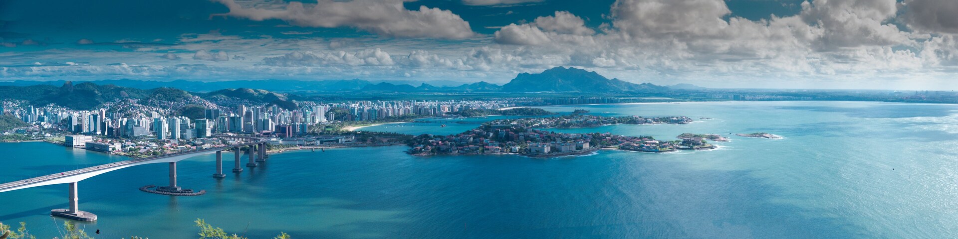 Paisagem costeira urbana com uma ponte imponente, área densamente construída e uma grande extensão de água com ilhas.