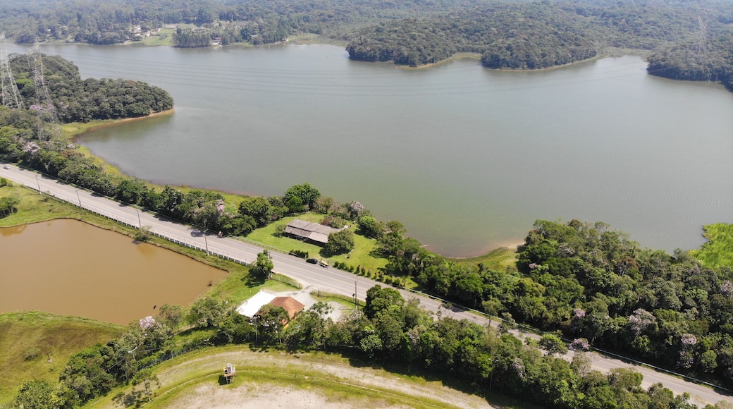 A large lake surrounded by dense forest, a road, and a small building.