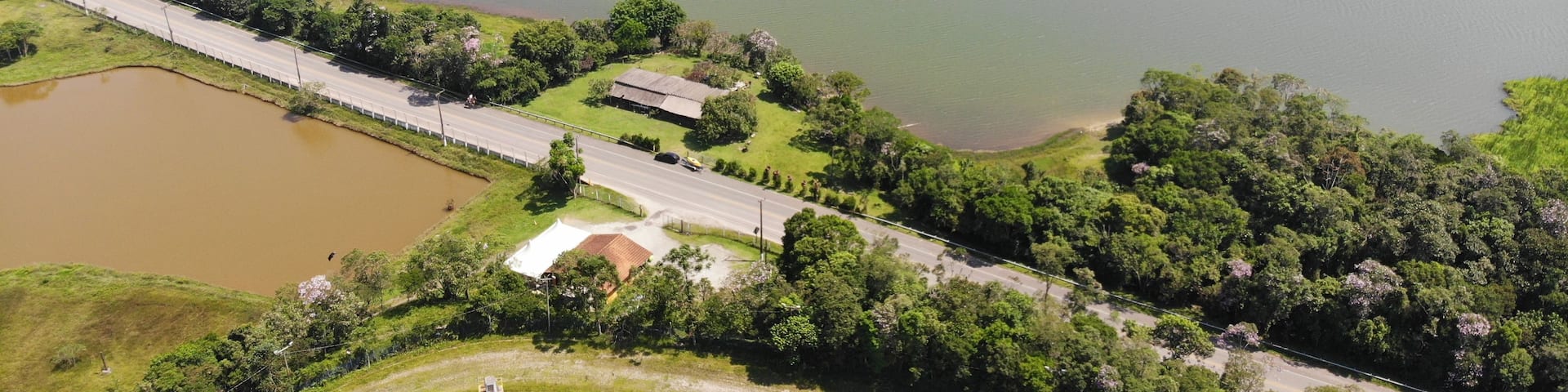 A large lake surrounded by dense forest, a road, and a small building.