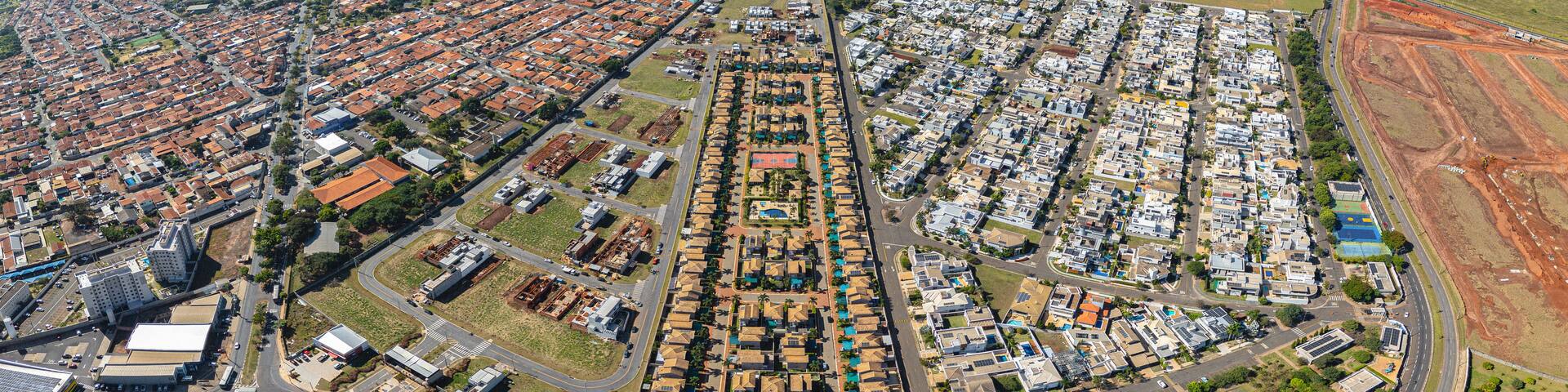 An aerial view of a city with dense residential areas, a large open field, and a distant body of water.
