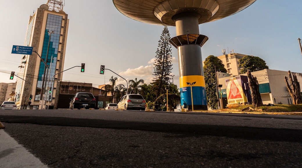 A large satellite dish structure, a tall building with a visible antenna, and a road with traffic lights and vehicles.