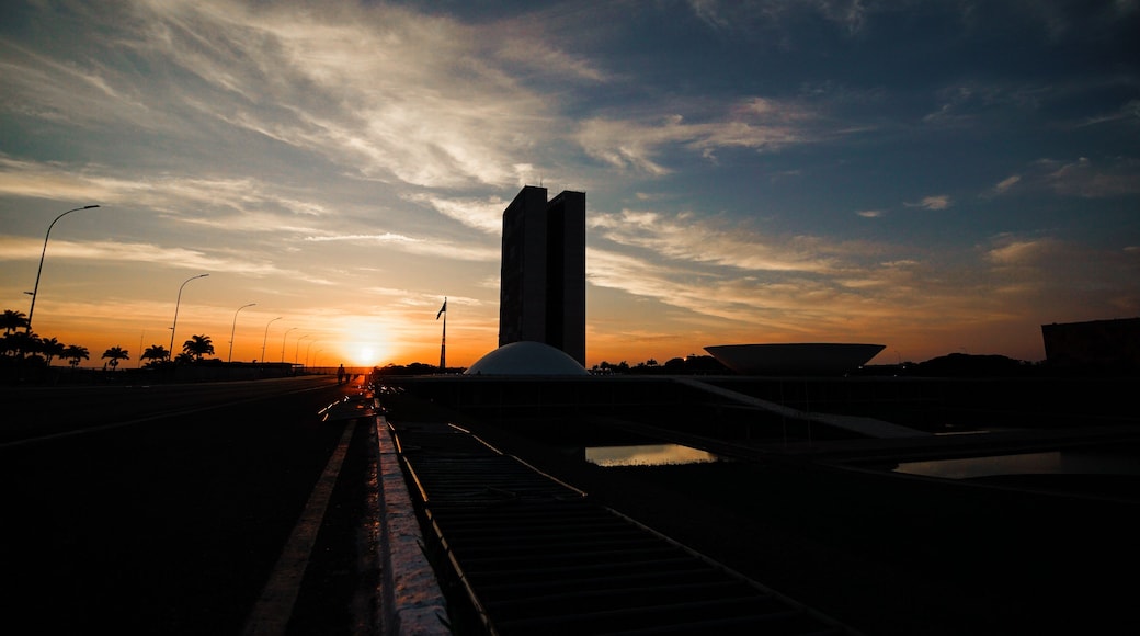 Un atardecer sobre un puente con un edificio alto y palmeras al fondo.