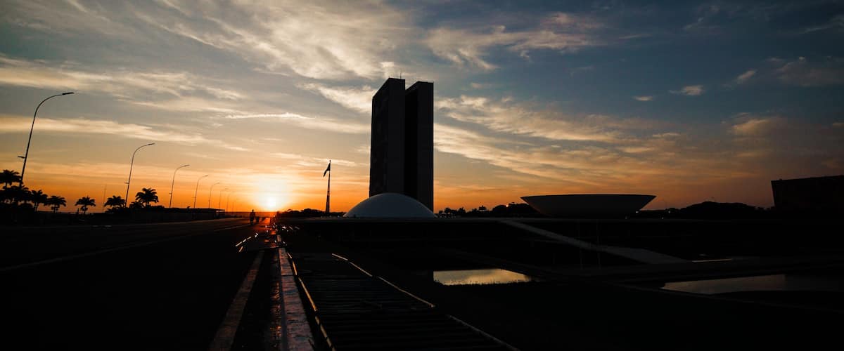Un atardecer sobre un puente con un edificio alto y palmeras al fondo.