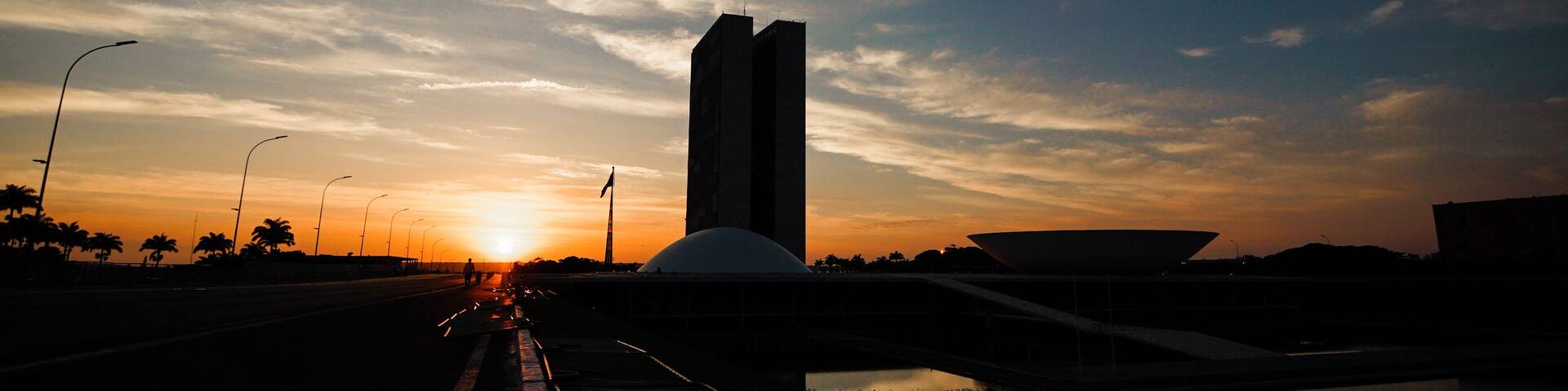 A sunset over a bridge with a tall building and palm trees in the background.