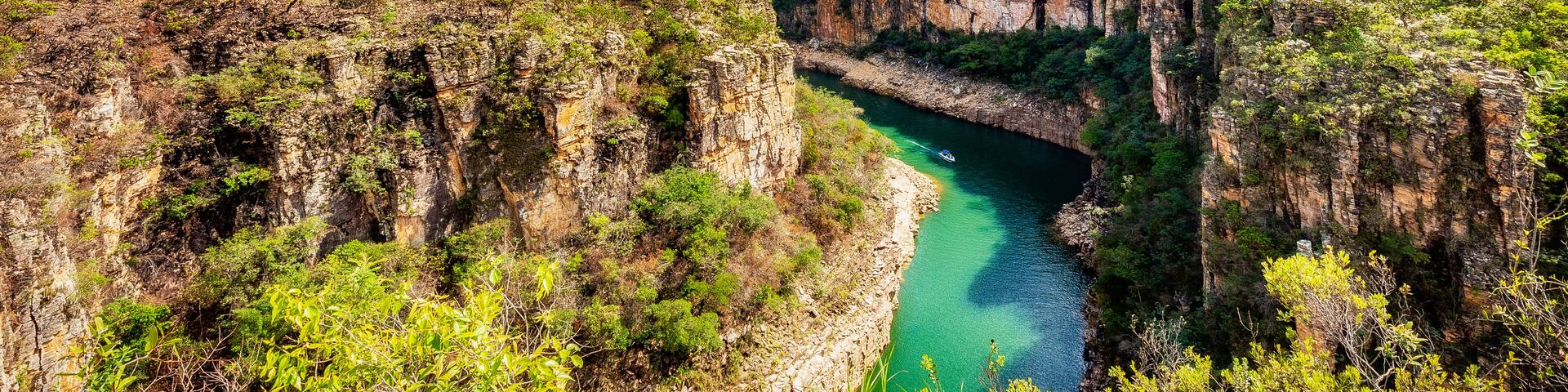 A canyon with a river, green vegetation, and a clear blue sky.