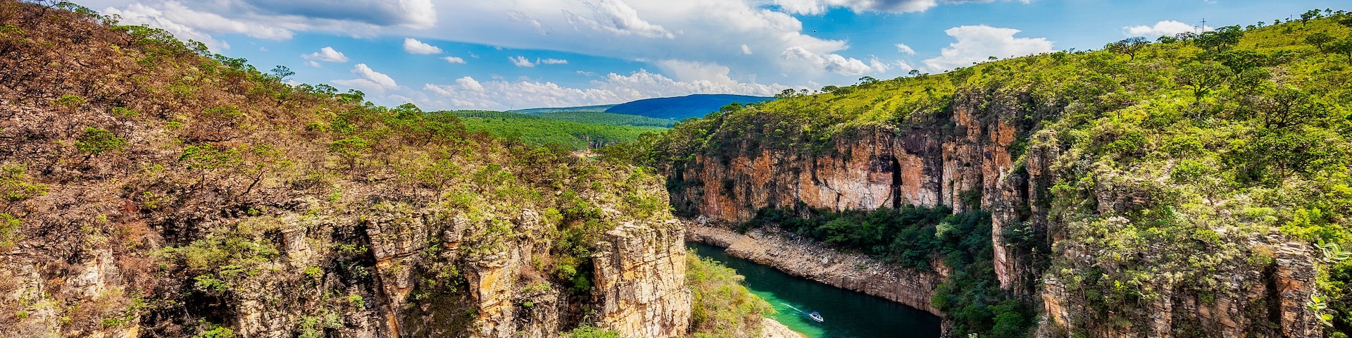 A canyon with a river, green vegetation, and a clear blue sky.