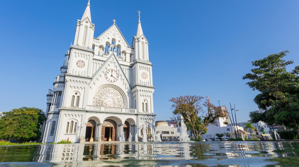 Une cathédrale blanche, dotée d’une grande horloge et de trois flèches, qui se reflète dans une étendue d’eau.