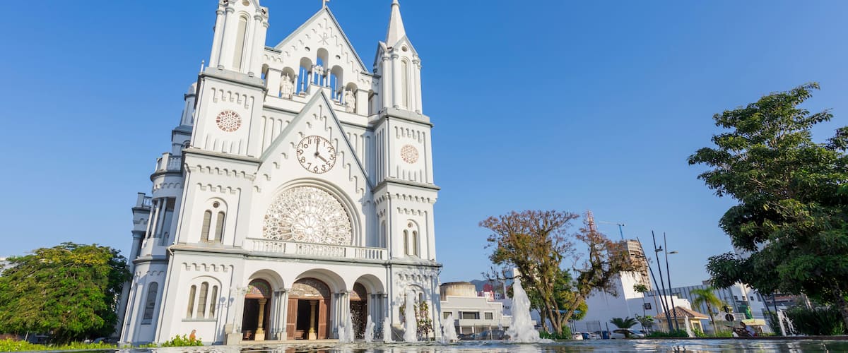 Uma catedral branca com um grande relógio e três torres, refletindo na água.