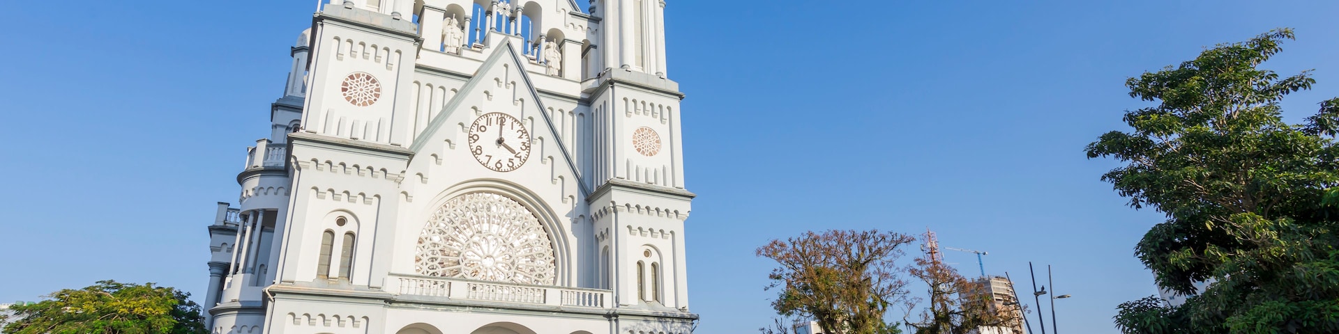 Uma catedral branca com um grande relógio e três torres, refletindo na água.