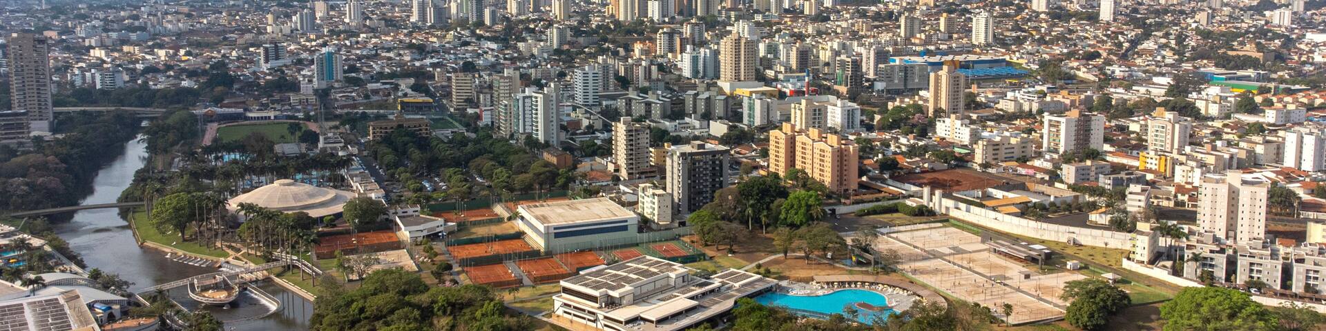 A densely populated urban area with high-rise buildings, a river, and a large public swimming pool surrounded by greenery.
