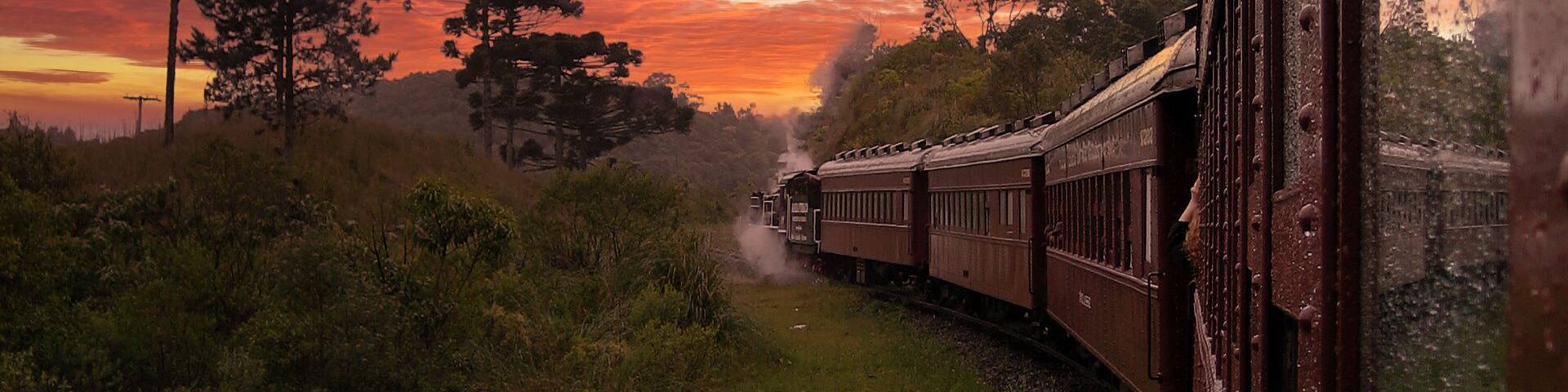 A train traveling through a rural landscape with a dramatic sunset sky.