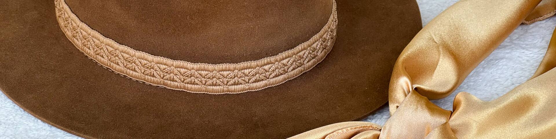 A brown hat with a braided band and a gold ribbon tied around it.