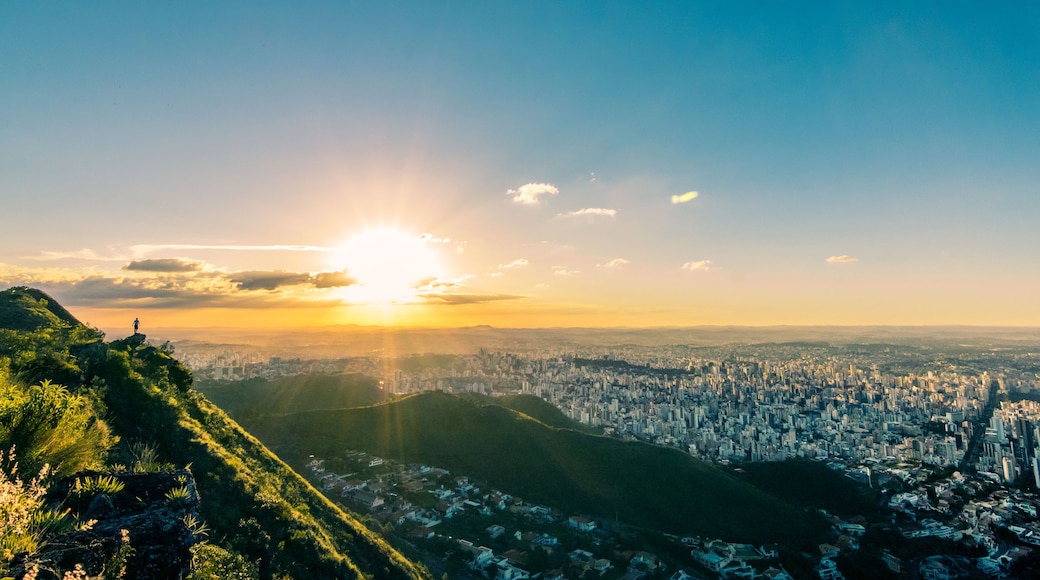Paisagem urbana com uma montanha ao primeiro plano e o sol se pondo ao fundo.