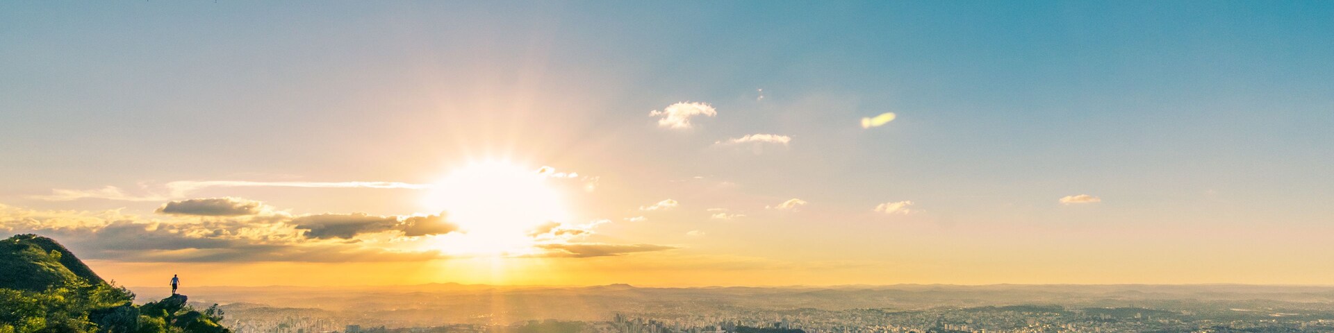 Paisagem urbana com uma montanha ao primeiro plano e o sol se pondo ao fundo.