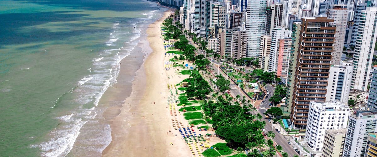 Paisagem costeira urbana com uma praia repleta de guarda-sóis coloridos e edifícios altos.