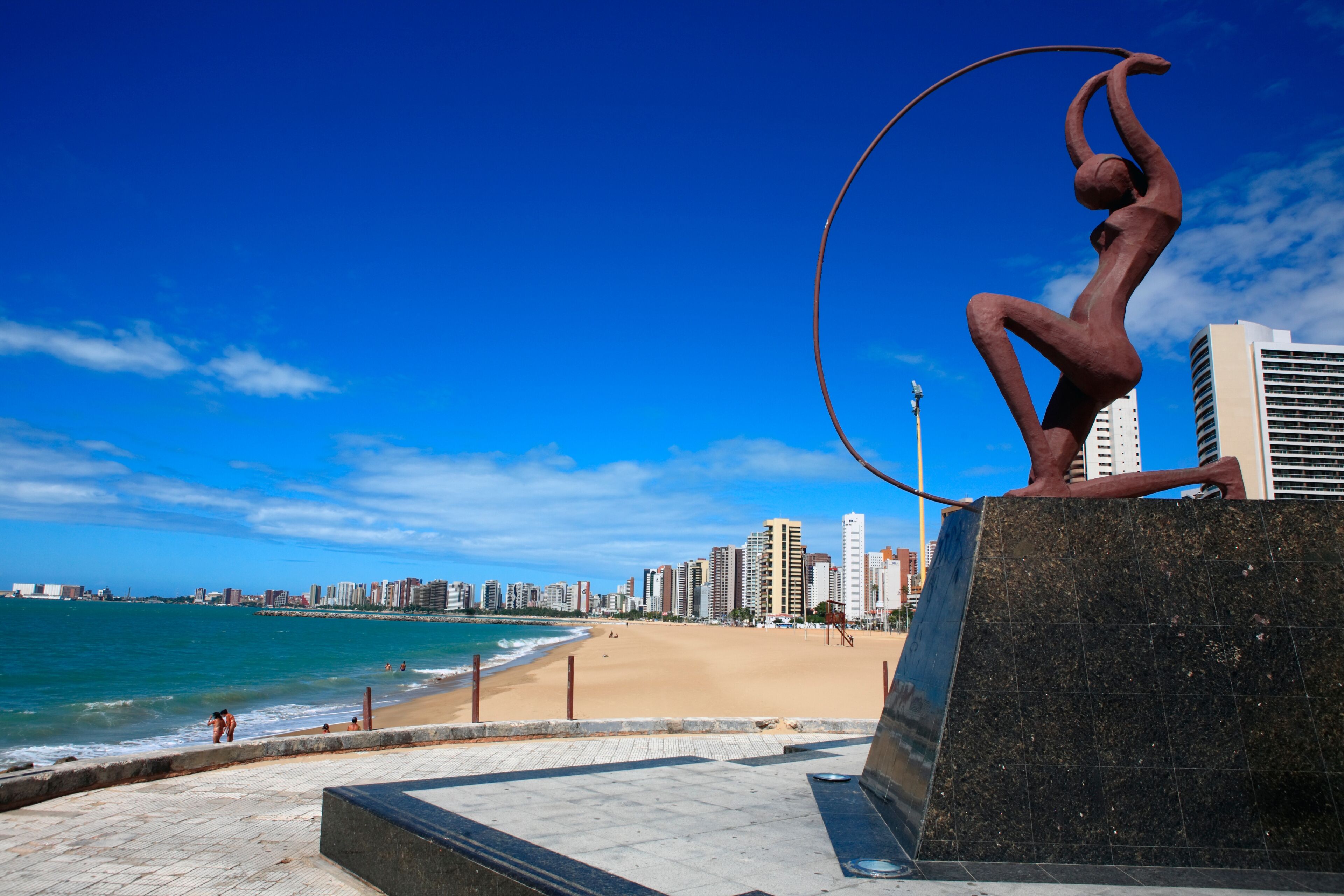 A beach with a sculpture of a figure holding a hoop.