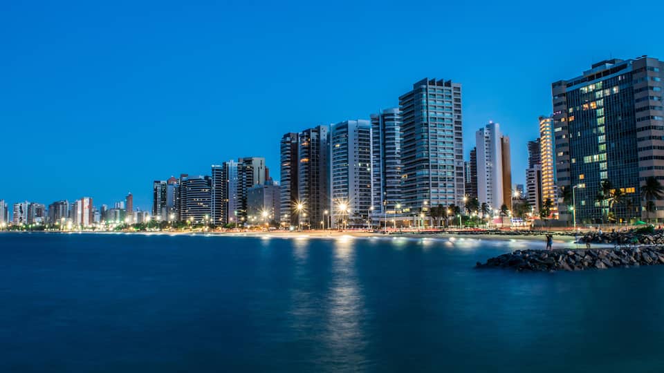 A city skyline at dusk with high-rise buildings along a waterfront.