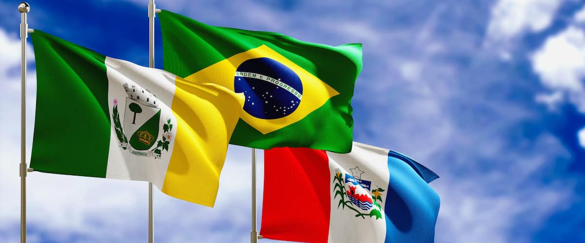 Varias banderas nacionales en mástiles frente a un cielo azul con nubes.