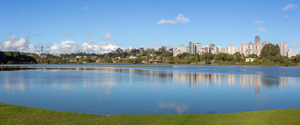 Barigui Park lake and island in Curitiba, Parana, Brazil, showcasing the modern city skyline against a bright blue sky.