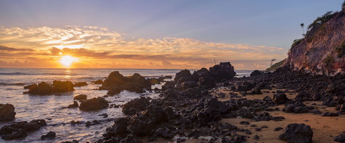 Uma costa rochosa com o sol se pondo sobre o oceano.