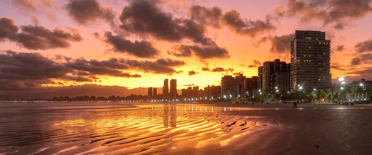 Um pôr do sol sobre uma praia com o horizonte da cidade ao fundo.
