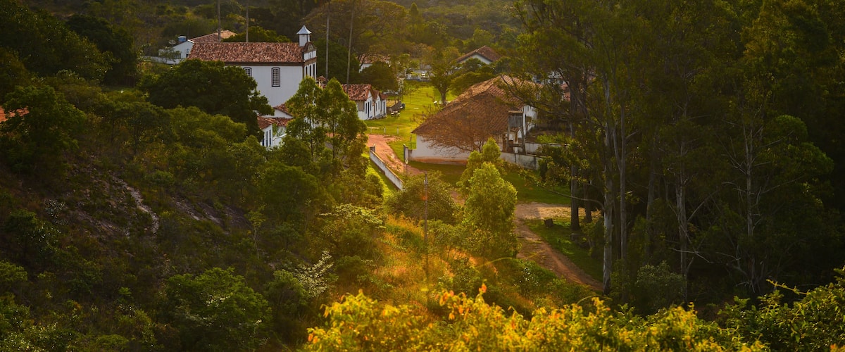 Uma vila aninhada em um vale, com vegetação exuberante e uma igreja imponente com telhado de telhas vermelhas.