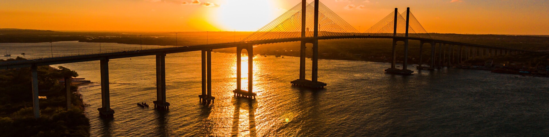 A suspension bridge at sunset with the sun setting behind it.