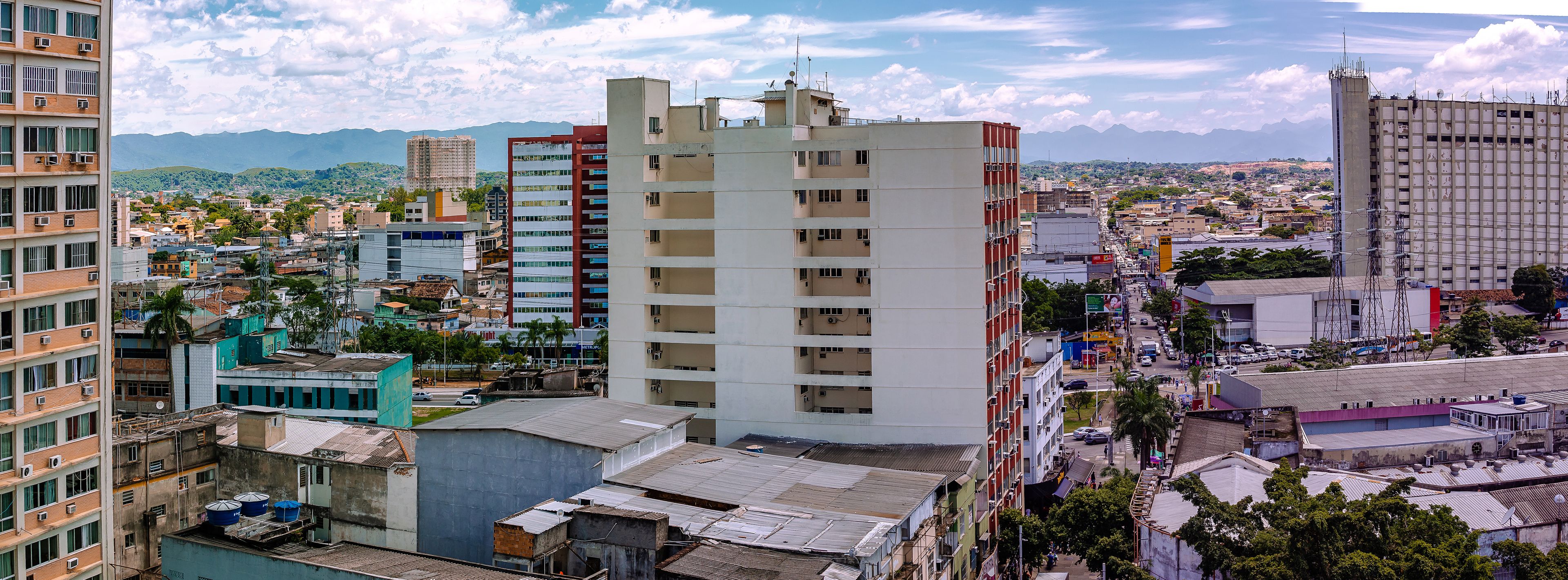 Un paisaje urbano con una mezcla de edificios modernos y antiguos, una calle con mucho tránsito y montañas al fondo.