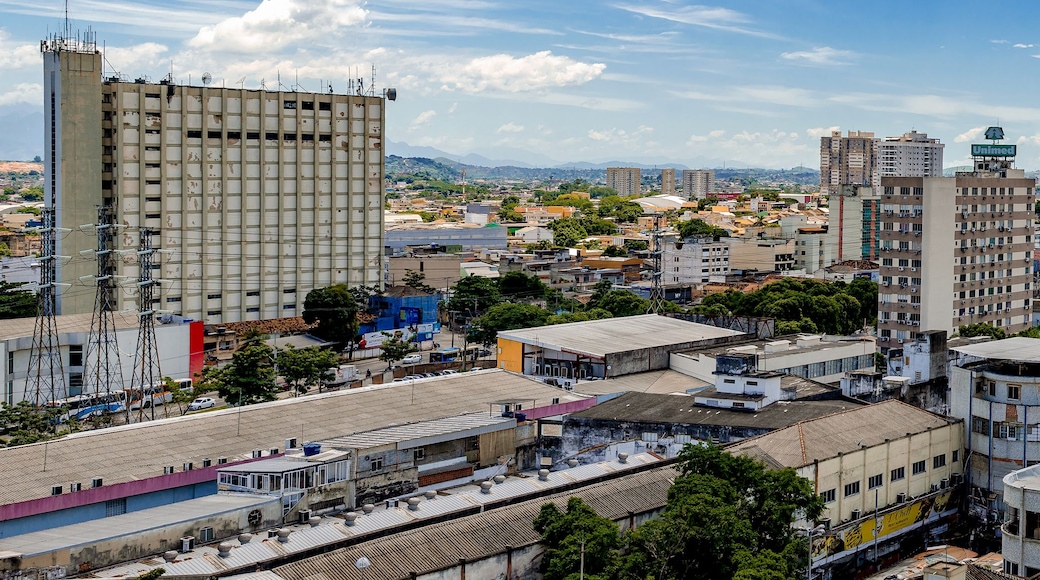 A cityscape with a mix of high-rise buildings and smaller structures, a clear sky, and distant mountains.