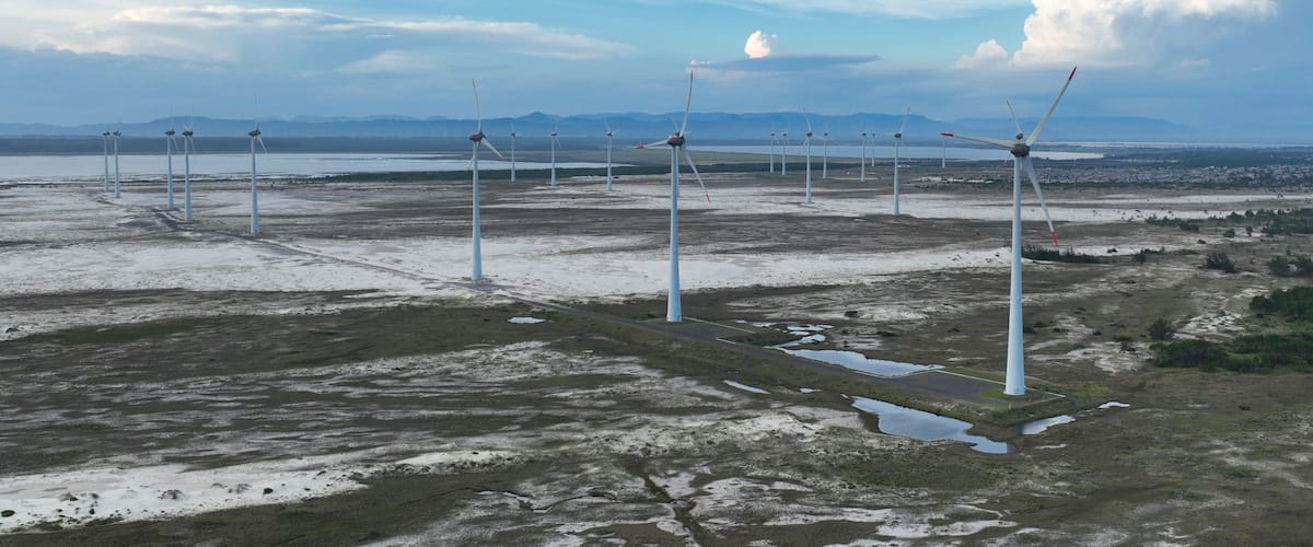 Een windmolenpark met meerdere windturbines in een vlak landschap met bergen in de verte.